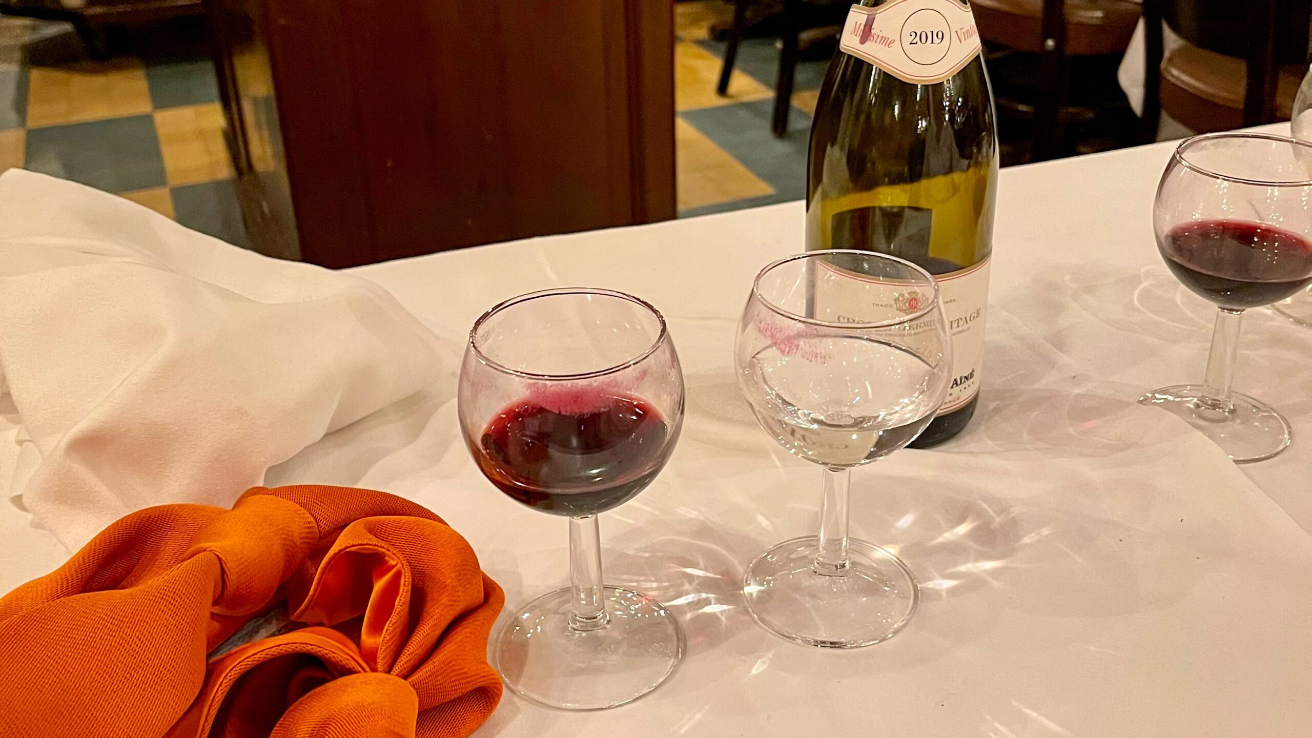 Vinflaske og glass med rødvin på et bord, dekorert med oransje stoff.