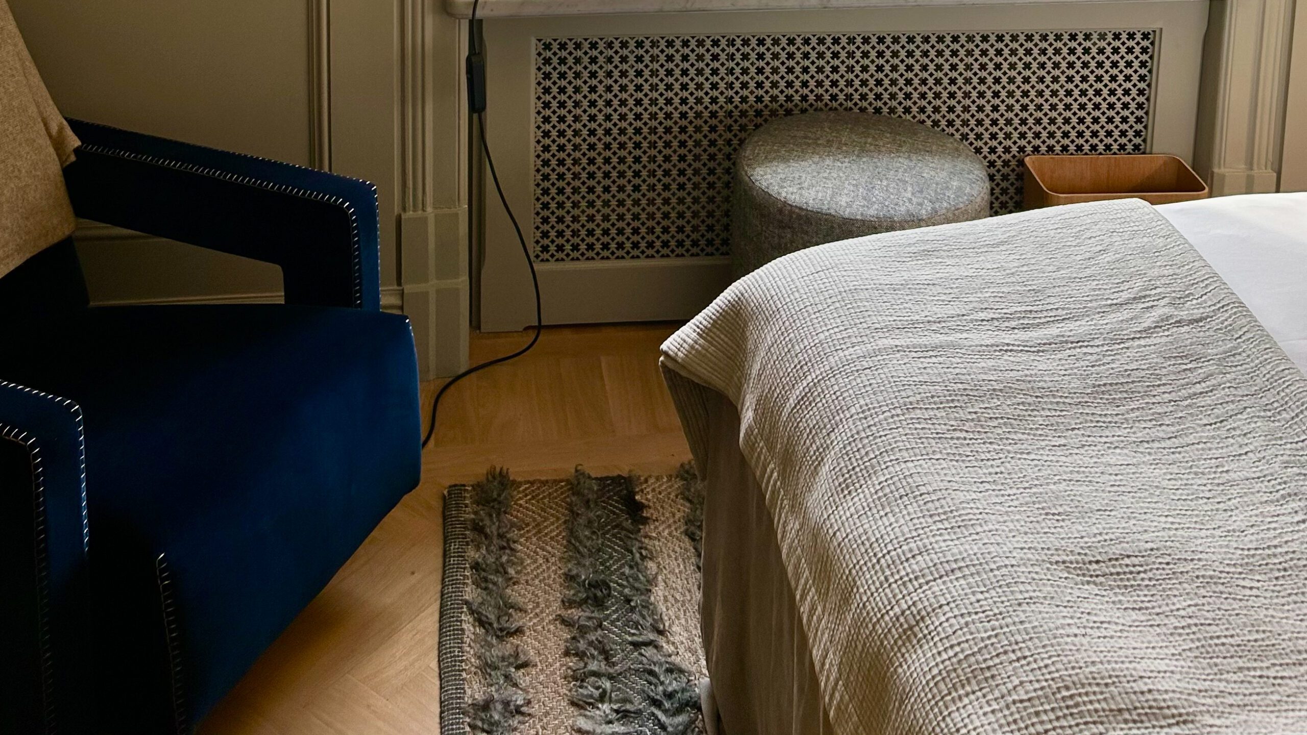 Moderne interiør med blå stol, seng med sengeteppe, dekorativ radiator, og lagdelt teppe på tregulv.