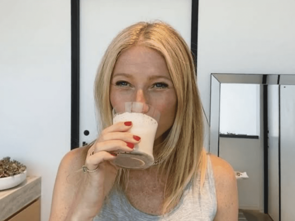 Kvinne med langt blondt hår drikker fra et glass med skummende drikke.