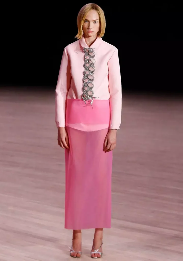 Modell iført rosa drakt med dekorativ detalj på skjorten på en falle.